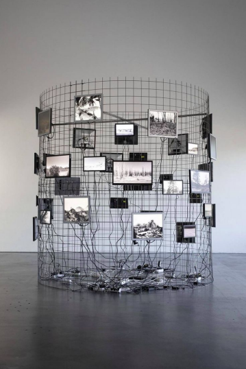 Cylindrical steel mesh structure hung with many small screens and trailing cables