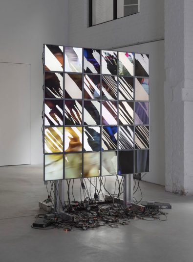 Freestanding tiled wall of many mismatched monitors with cables pooling on the floor